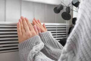 Hands warming near a home heater vent when turning heat on for the first time in winter