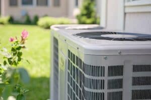 Outdoor residential air conditioning condenser unit installed beside a home, surrounded by grass and landscaping, representing spring AC maintenance and seasonal HVAC system care.