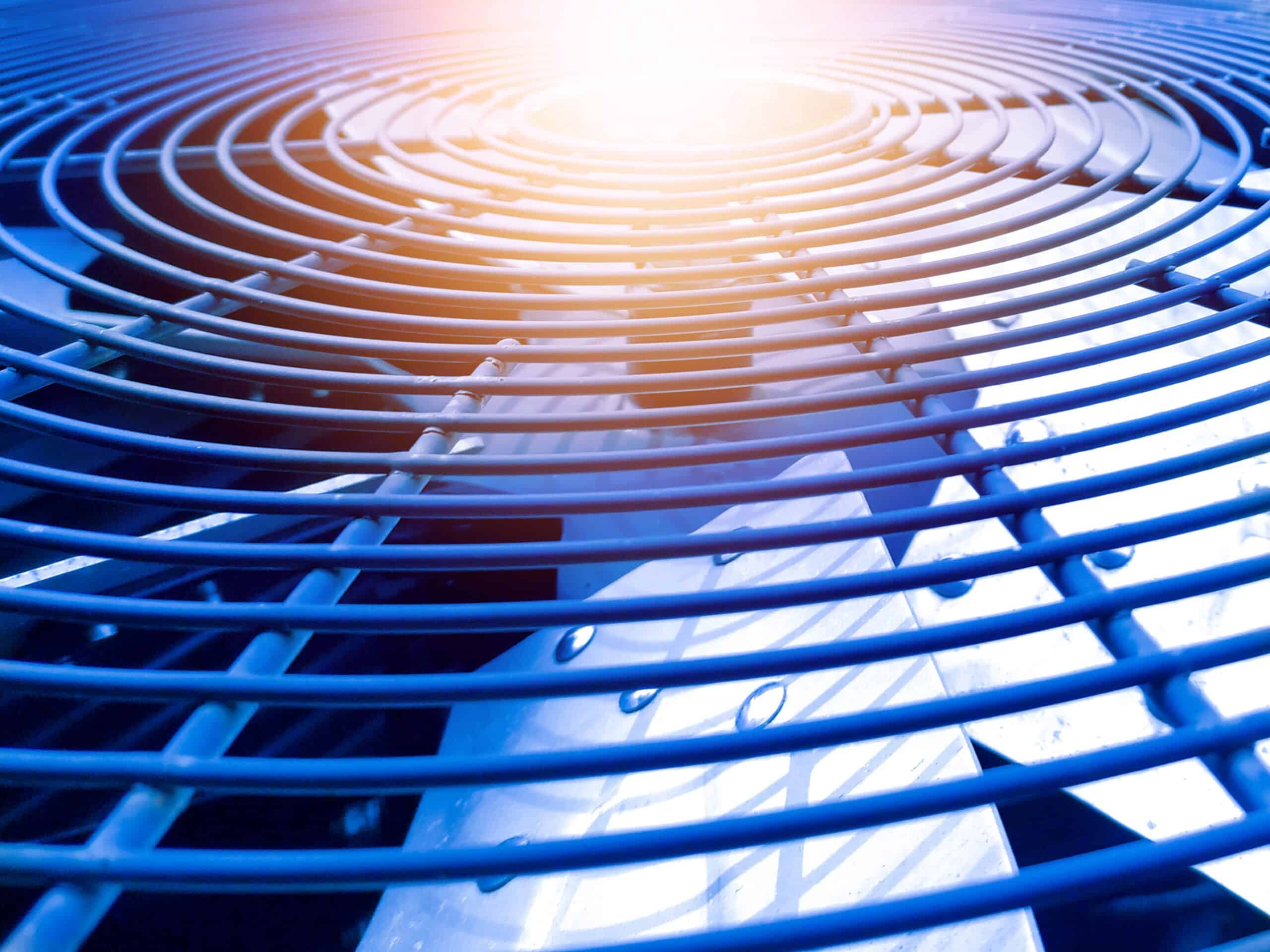 Close-up of a commercial HVAC unit fan grille with sunlight reflecting across metal coils and blades.